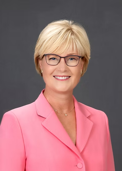 Woman with blonde hair and glasses wearing pink suit jacket