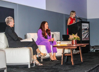 Woman in red dress at podium, with two other women seated on couches