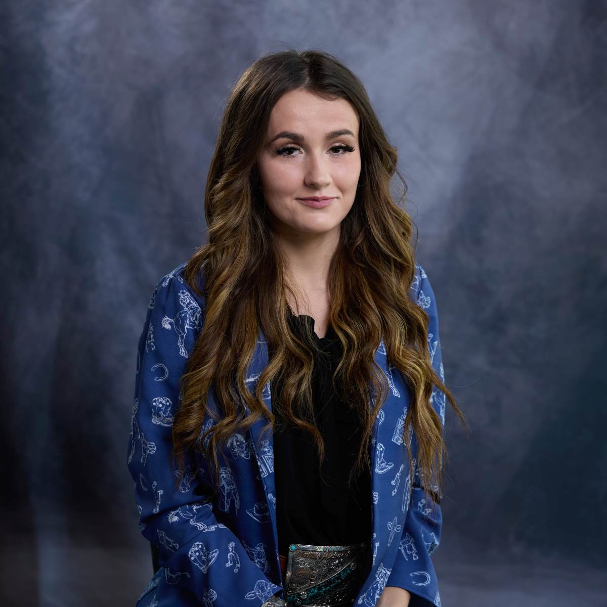 Woman with long wavy hair wearing blue shirt over black polo.